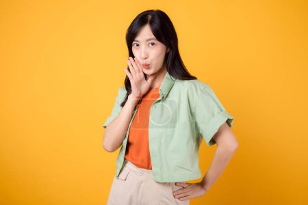 Eine junge Asiatin in den 30er Jahren, die ein grünes Hemd auf orangefarbenem Grund trägt und begeistert vor Begeisterung schreit. Entdecken Sie das Konzept der Discount-Shopping-Förderung mit diesem lebendigen Image.