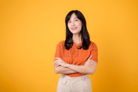 Photo for Discover the power of confidence with a young Asian woman 30s, dressed in an orange shirt, displaying crossed arm sign gesture on yellow background. - Royalty Free Image