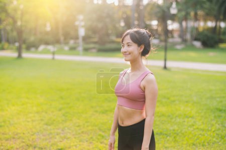 Foto de Experimenta la alegría de una corredora femenina feliz y en forma de los años 30. Mujer asiática vestida con ropa deportiva rosa, disfrutando del aire fresco en un parque público. Abrace la vida de bienestar y conéctese con la naturaleza. - Imagen libre de derechos