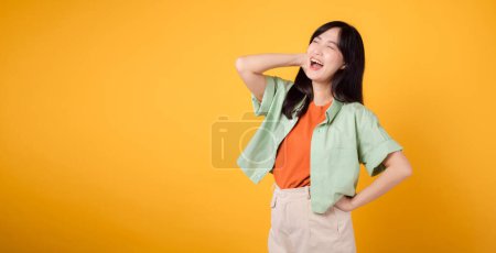 Photo for Essence of happiness and well-being with cheerful young Asian woman 30s wearing an orange shirt. Her happy mind wellness gesture on yellow background illuminates compelling happiness portrait. - Royalty Free Image
