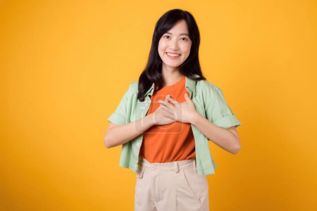 Téléchargez les photos : Vivez la joie de l'épargne avec une jeune femme asiatique heureuse trentaine portant une chemise verte sur fond jaune vif. Love deal concept de promotion! - en image libre de droit