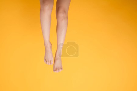 Téléchargez les photos : Découvrez le charme du toucher lisse et doux avec les jambes rapprochées d'une personne élégante des années 30 sur une toile de fond jaune vif. Concept de pied doux et velouté. - en image libre de droit