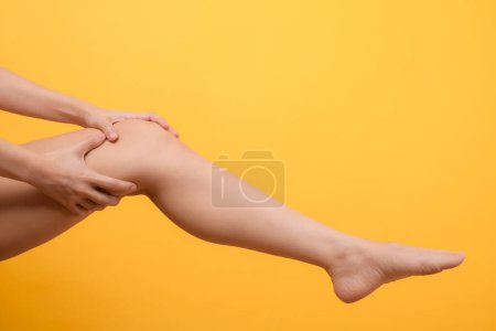 Téléchargez les photos : Douleur au genou, les mains de la femme tenant le genou isolé sur fond jaune. jambes et genou concept de soins de santé. - en image libre de droit