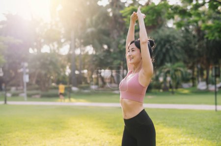 Téléchargez les photos : Bien-être et mode de vie sain portrait de femme asiatique 30s en vêtements de sport rose. préparer et étirer les muscles des bras avant le coucher du soleil dans le parc. forme physique à l'extérieur et vivre une vie équilibrée. - en image libre de droit