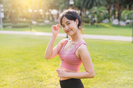 Téléchargez les photos : Vivez la joie de vivre bien-être comme une jeune femme asiatique heureuse 30s sourit à la caméra dans un parc au coucher du soleil. Adoptez la beauté de la nature et un mode de vie sain. - en image libre de droit