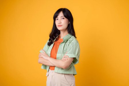 Téléchargez les photos : Portrait de confiance rayonnant de la jeune femme asiatique porte une chemise vert pastel sur chemise orange croisant avec confiance ses bras. Parfait pour capturer un sentiment d'assurance et d'autonomisation. - en image libre de droit