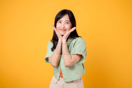 Photo for A young Asian woman 30s wearing a green shirt on an orange shirt radiates joy with a happy face. Discover the vibrant energy of cheerful image on a yellow background. - Royalty Free Image