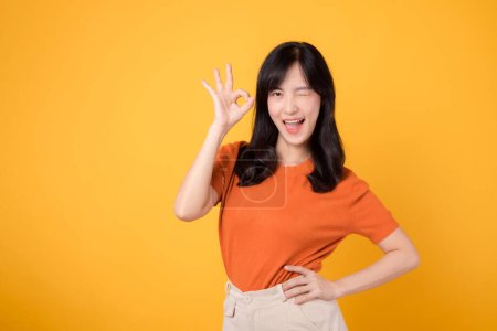 Photo for Young 30s asian woman wearing orange shirt showing okay sign gesture isolated on yellow background. Female person with hands gesture concept. - Royalty Free Image