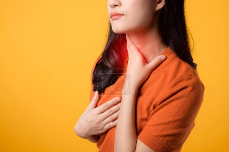 Photo for Caring young Asian woman 30s, wearing an orange shirt, holds her pain neck on yellow background. - Royalty Free Image