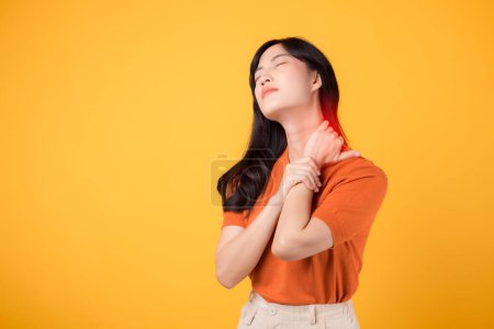 Téléchargez les photos : Femme asiatique de soutien trentaine, portant une chemise orange, tient son cou douloureux sur fond jaune. syndrome de bureau concept de soins de santé. - en image libre de droit
