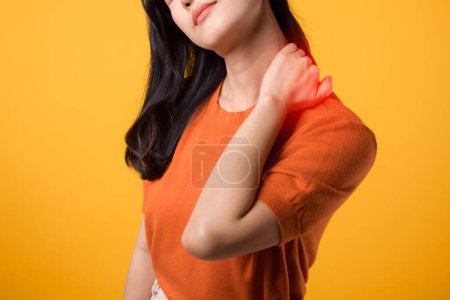 Foto de Mujer asiática preocupada de 30 años, vistiendo una camisa naranja, sostiene su dolor en el cuello sobre un fondo amarillo. síndrome de oficina concepto de atención médica. - Imagen libre de derechos