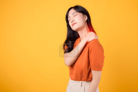 Photo for Young 30s asian woman wearing orange shirt holding her pain shoulder isolated on yellow background. office syndrome health care concept. - Royalty Free Image