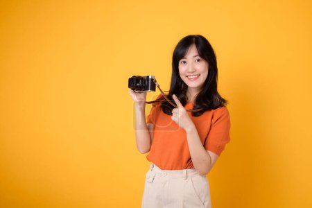 Téléchargez les photos : Femme vibrante avec caméra isolée sur fond jaune, montrant l'aventure d'explorer de nouveaux endroits pendant ses vacances. - en image libre de droit