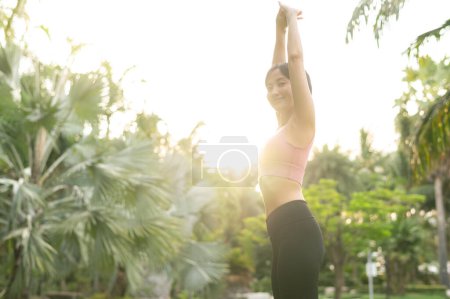 Foto de Bienestar y bienestar en forma joven mujer asiática de 30 años en ropa deportiva rosa se dedica al yoga y estira los músculos. Adopta un estilo de vida saludable al aire libre con esta chica de yoga fitness en un parque público al atardecer. - Imagen libre de derechos