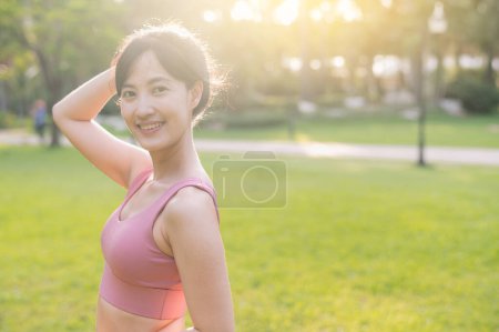 Téléchargez les photos : Joyeux joggeuse. jeune belle asiatique femme 30s regardant un appareil photo et sourire dans le parc au coucher du soleil. concept de vie bien-être. - en image libre de droit