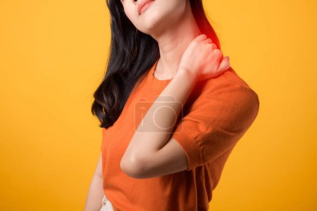 Photo for Attentive young Asian woman 30s, wearing an orange shirt, holds her pain neck on yellow background. office syndrome health care concept. - Royalty Free Image