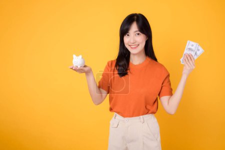 Photo for Energetic Asian woman 30s holding piggy bank and cash money dollars on vibrant yellow background. Financial success concept. - Royalty Free Image