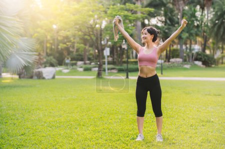 Téléchargez les photos : Vivez le bien-être d'une joggeuse des années 30. Femme asiatique vêtue de vêtements de sport roses, respirant l'air frais dans un parc public. Adoptez un concept de vie bien-être inspiré de la nature - en image libre de droit