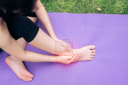 Téléchargez les photos : Sportive tenant sa cheville de douleur après avoir fait de l'exercice sur tapis de yoga dans le parc extérieur. accident de blessure dans le concept d'exercice. - en image libre de droit