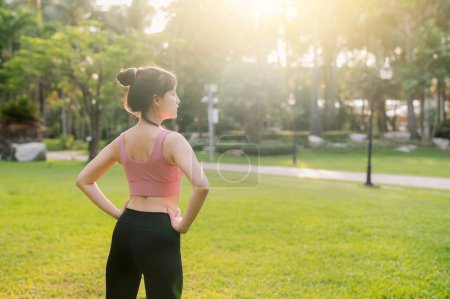 Foto de Abrace el bienestar que vive en la naturaleza como una mujer asiática feliz, en forma de los años 30 calienta su cuerpo en un parque público antes de una puesta de sol, usando ropa deportiva rosa. - Imagen libre de derechos