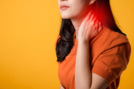 Foto de Joven mujer asiática de 30 años con camisa naranja sosteniendo su cuello dolorido aislado sobre fondo amarillo. síndrome de oficina concepto de atención médica. - Imagen libre de derechos