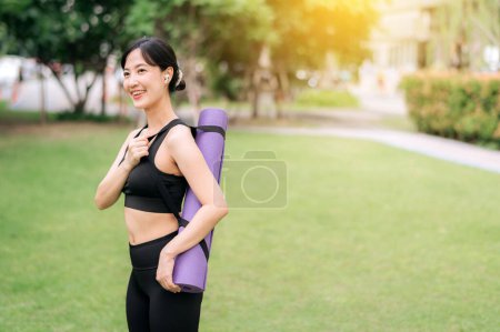 Photo for Portrait of young asian slim and healthy girl prepared doing workout in park, standing with rubber mat before exercises on green park at sunset, healthcare and well-being and yoga concept. - Royalty Free Image