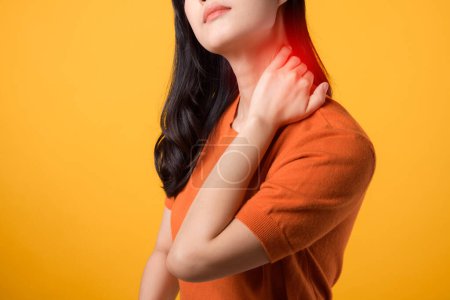 Photo for Aware Asian woman 30s, wearing an orange shirt, holds her pain neck on yellow background. office syndrome health care concept. - Royalty Free Image