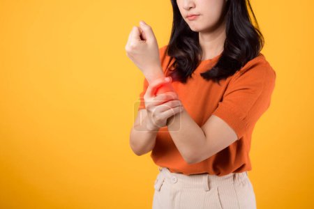 Téléchargez les photos : Jeune femme debout avec un poignet douloureux isolé sur fond jaune, mettant en valeur la douleur de l'arthrite. Portrait d'une personne souffrant de douleurs au poignet. - en image libre de droit