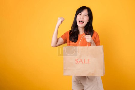 Photo for Join the celebration of love and incredible deals for joyful shopping experience. Trendy asian woman reveals purchases, embodying the excitement of smart shopping. isolated on yellow background. - Royalty Free Image