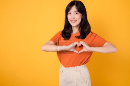 Téléchargez les photos : Jeune femme asiatique trentaine portant chemise orange montrant geste de la main du cœur sur la poitrine isolée sur fond jaune. concept de santé, bien-être et bien-être. - en image libre de droit