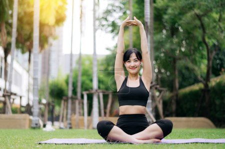 Photo for Portrait fit young asian woman wearing black sportswear listen relaxing music while stretching muscle before yoga exercise on yoga mat in green nature park. wellbeing concept. - Royalty Free Image