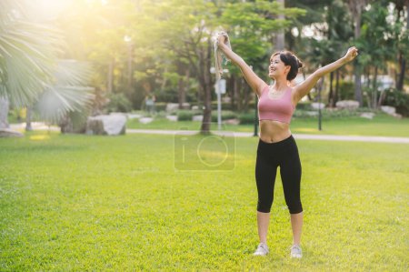 Téléchargez les photos : Joyeux jogging féminin. Femme asiatique trentaine portant des vêtements de sport roses respirant l'air frais dans le parc public. Wellness living et concept nature. - en image libre de droit