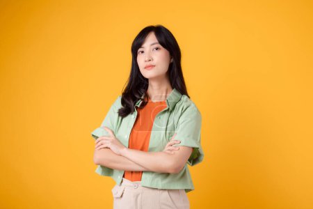 Foto de Radiar confianza retrato de mujer joven asiática lleva camisa verde pastel en camisa naranja con confianza cruzando sus brazos. Perfecto para capturar un sentido de seguridad en sí mismo y empoderamiento. - Imagen libre de derechos