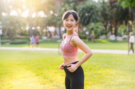Téléchargez les photos : Vivez la joie de vivre bien-être comme une femme asiatique heureuse 30s sourit à la caméra dans un parc au coucher du soleil. Adopter un mode de vie sain et dynamique - en image libre de droit