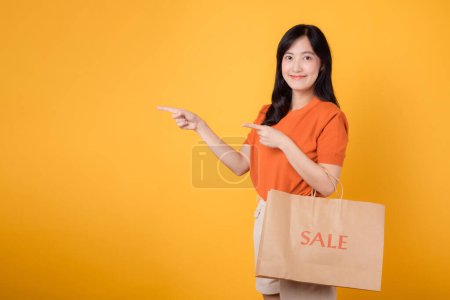 Photo for Happy young shopper celebrates thrill of discounts, pointing to free copy space while holding shopping bags with a joyful gesture. - Royalty Free Image