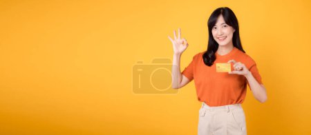 Téléchargez les photos : Belle dame asiatique montrant avec confiance une carte de crédit, mettant l'accent sur les achats en ligne sécurisés et les transactions financières - en image libre de droit