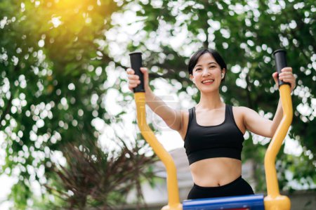Téléchargez les photos : Jeune sportive asiatique portant des vêtements de sport écoutant de la musique relaxante tout en travaillant sur l'équipement d'exercice en plein air dans le parc. Concept de mode de vie sain - en image libre de droit