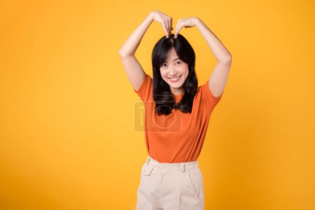 Photo for Expressive and genuine, a young Asian woman 30s showcases a heart gesture, embodying affection and joy, against a vibrant backdrop. - Royalty Free Image