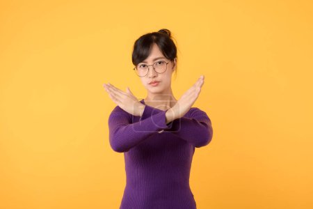 Photo for Portrait Asian beautiful young woman 30s unhappy wear purple shirt holding two cross arms say no X sign, studio shot isolated yellow background, female model pose reject gesture with copy space - Royalty Free Image