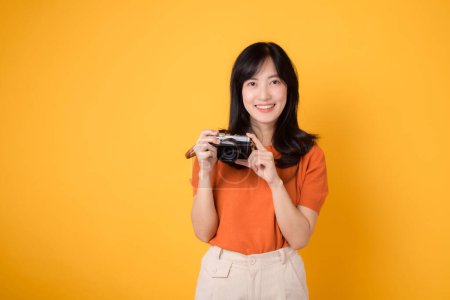 Téléchargez les photos : Jeune femme asiatique avec caméra, prête pour une visite d'aventure amusante. Ambiances de vacances positives sur un fond jaune - en image libre de droit