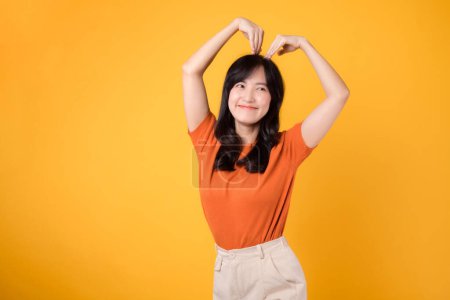 Téléchargez les photos : Chaleur et authenticité brillent comme une femme asiatique joyeuse dans la trentaine embrasse l'amour avec un geste en forme de cœur et un sourire contagieux. - en image libre de droit