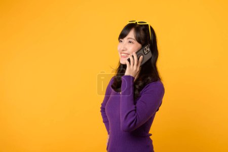 Téléchargez les photos : Portrait jeune femme asiatique portant un pull violet s'exprimant à l'aide d'un téléphone portable isolé sur fond jaune. Connection, communication, conversation concept technologique. - en image libre de droit