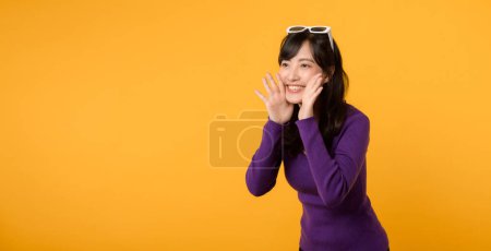 Téléchargez les photos : L'excitation abonde en tant que dame à la mode, dans une chemise violette et des lunettes de soleil sur un fond jaune, délivre un message vivant et positif avec des gestes vibrants et une expression heureuse. - en image libre de droit