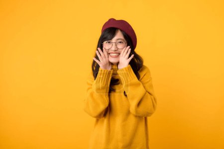 Photo for Stylish woman, in a yellow sweater and red beret, shouts an announcement against a vibrant yellow background. - Royalty Free Image