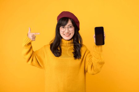 femme donnant un pouce vers le haut, en utilisant un smartphone, et portant un béret rouge élégant et des lunettes sur un fond jaune vif.
