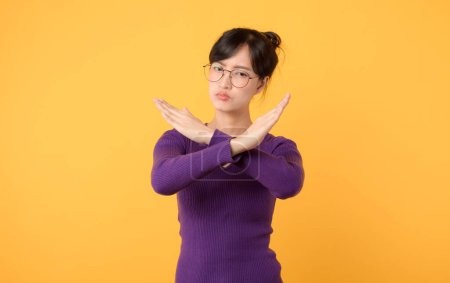 Photo for A portrait young lady wearing a purple shirt and eyeglasses, using X gesture with arms, indicating negative or forbidden action. Seriousness and caution evident expression against a yellow background. - Royalty Free Image