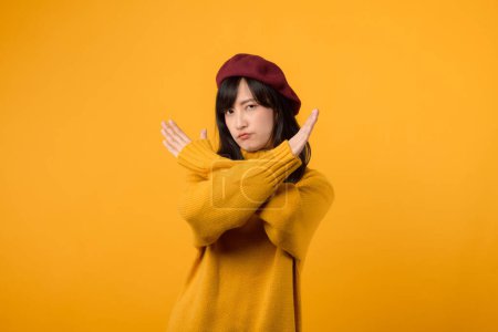 Téléchargez les photos : Jeune femme asiatique trentaine, portant un pull jaune et béret rouge, affiche un signe d'arrêt sérieux sur un fond jaune vif. - en image libre de droit
