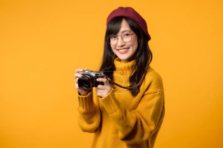 Una fotógrafa profesional, joven asiática, abraza su pasión con una cámara, irradiando alegría y creatividad en su suéter amarillo y boina roja.