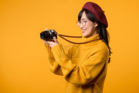 Téléchargez les photos : Habillée d'un pull jaune et d'un béret rouge, la jeune femme asiatique manipule artistiquement son appareil photo alors qu'elle poursuit sa passion pour la photographie et les voyages. - en image libre de droit
