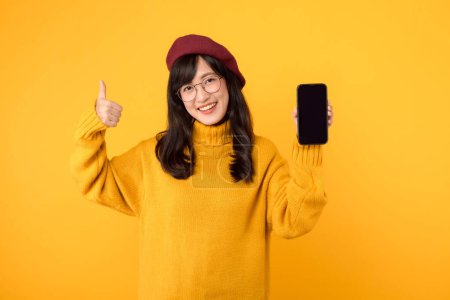 Photo for Ethnic woman with a smartphone, showcasing a thumb up gesture, in a trendy yellow setting, wearing a red beret and eyeglasses. - Royalty Free Image